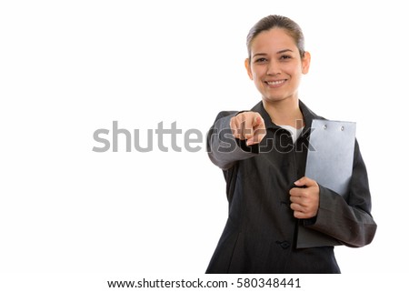 Studio shot of young happy businesswoman smiling holding clipboard while pointing at camera