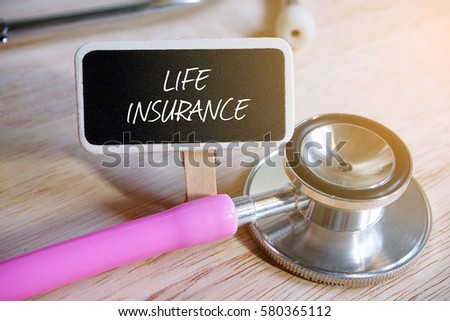 Pink stethoscope and blackboard written with LIFE INSURANCE on wooden background.
