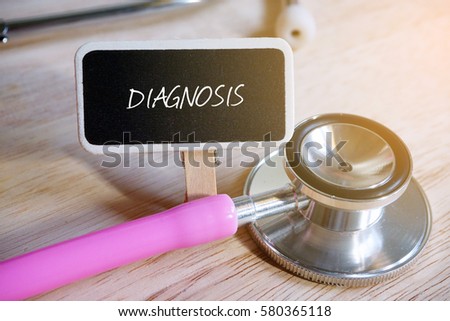 Pink stethoscope and blackboard written with DIAGNOSIS on wooden background.