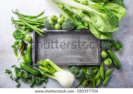 Background with assorted green vegetables and old wooden tray on light gray stone table top. Healthy food concept with copy space.