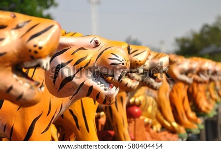 Side profile view of a row of tiger statues lined up at the side of a religious Spirit House in Thailand. This is a shrine where local people will light incense and present offerings each day. 