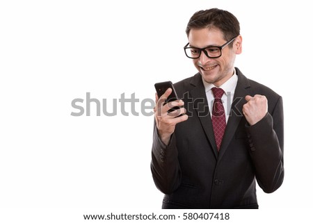 Studio shot of happy young businessman smiling while using mobile phone and looking motivated