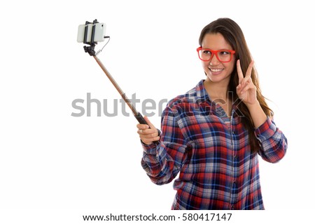 Young happy woman smiling while taking selfie picture with selfie stick and giving peace sign
