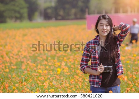 Outdoor summer smiling lifestyle portrait of beautiful young woman having fun in the cosmos flower field with camera travel photo of photographer Making pictures in hipster style