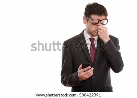 Studio shot of tired young businessman wearing eyeglasses while holding mobile phone