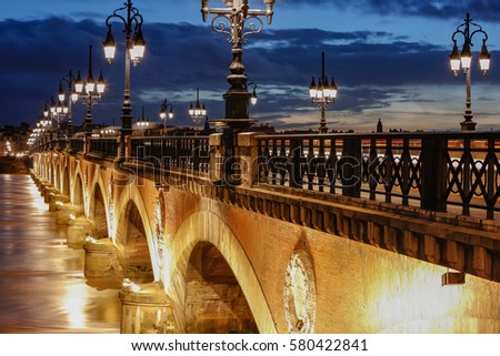 Pont de Pierre stone bridge on the river garonne in Bordeaux, France at sunset with the st michel church in the background