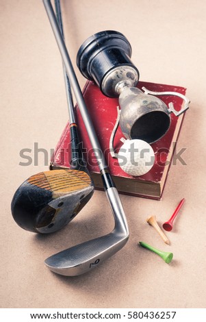 still life photography : golf club and golf ball and tee with old champion trophy and old book