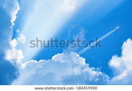 Airplane flying in the blue sky among clouds and sunlight Royalty-Free Stock Photo #580459900