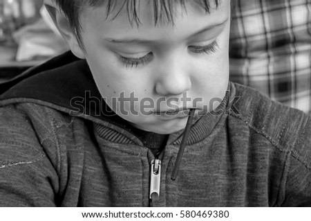 Cute Caucasian little boy with a lollipop candy looking down, busy playing, concentrated, black and white stock image.