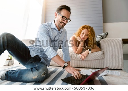 Energetic couple sitting and using laptop at home Royalty-Free Stock Photo #580537336