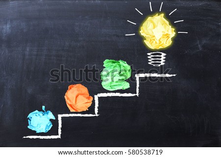 Evolving idea concept with colorful crumpled paper and light bulb on steps drawn on blackboard Royalty-Free Stock Photo #580538719