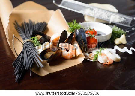Ingredients for making black pasta with mussels and shrimps,tomato sauce, spices and herbs. On dark wooden background.
