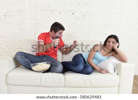 young couple watching tv sport football game with man excited celebrating crazy happy goal and wife or girlfriend bored and frustrated in relationship lifestyle concept