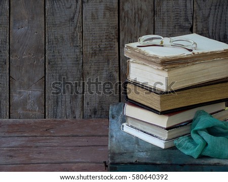 The composition of a stack of old books and glasses on a wooden background. Vintage photo. Side view. Copy space