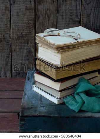 The composition of a stack of old books and glasses on a wooden background. Vintage photo. Side view