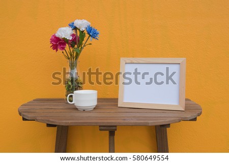 photo Frame and cup and Flowers in jar on a wooden on Yellow background .