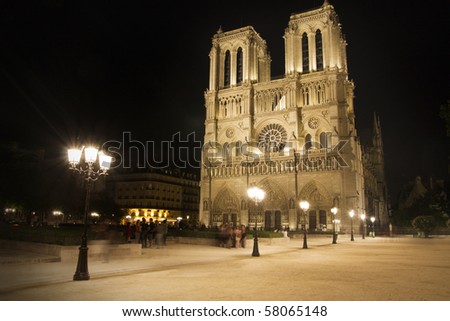 View of Notre Dame square in Paris with the famous cathedral  by night - unrecognizable blurred people and streetlamps on foreground.