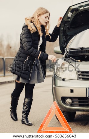 Auto assistance and insurance, troubles while traveling concept. Broken car and auto triangle on road, woman waiting for help.