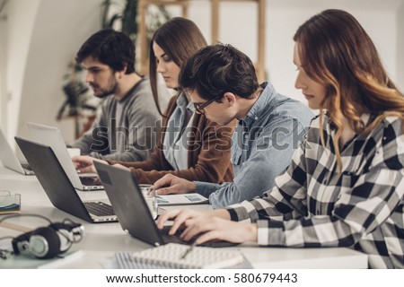 Group of male and female students sitting in classroom and studying on laptops.