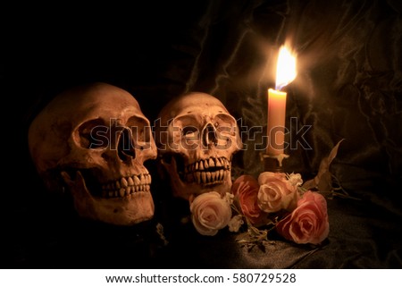 Two Human Skulls and flowers with light candle in dim valentines night on old wooden table / Still life Image
