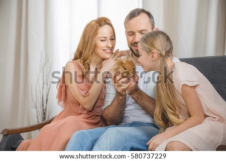 Happy family sitting on couch and playing with cute little rabbit
