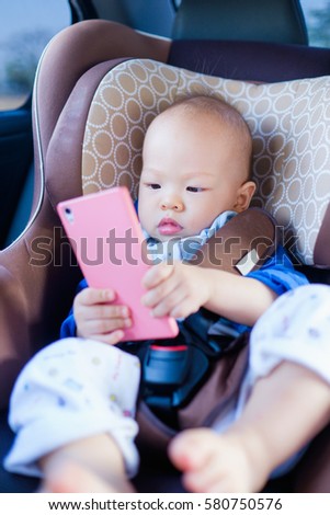 Cute asian toddler baby boy sitting in car seat and watching a video from smart phone. Kids playing in the car with smartphone. leisure & children & technology & internet addiction concept