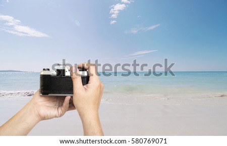 Man holding film camera ready to take photo over sea beach with blue sky background