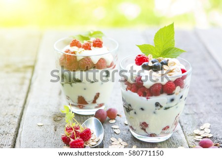 Delicous blackcurrant sundaes or desserts served outdoors of colorful layered, ice cream or frozen yoghurt, red raspberry, blackcurrants on wood table over green garden background