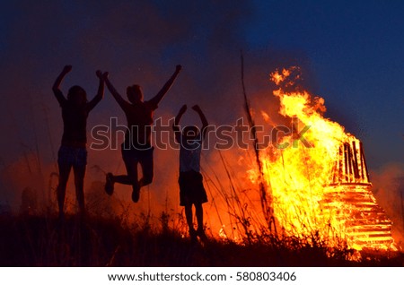 three happy young people standing and dancing in front of fire