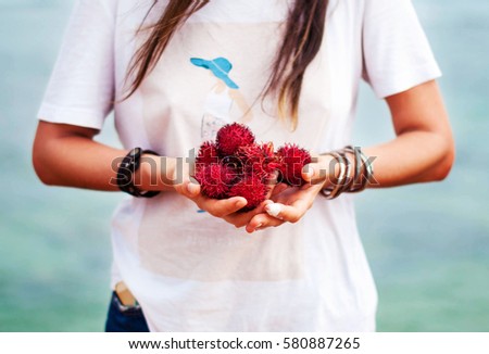 The fruits of litchi in the hands of a girl with bracelets on background of ocean. Girl holds in the hands of lychee.