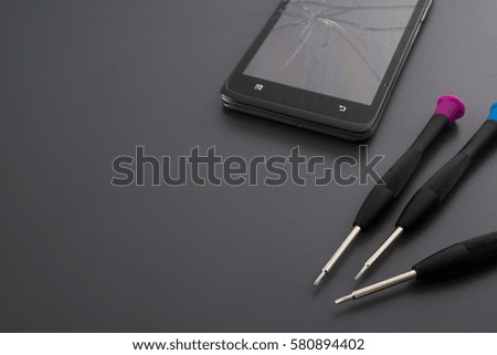 Broken smartphone and small screwdrivers for repair on grey background.