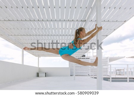 Gymnast on the beach. Female gymnast performs leg split in a contemporary place. Teenage sportsman. Sportswoman. Teenage sport. Teenage gymnast.