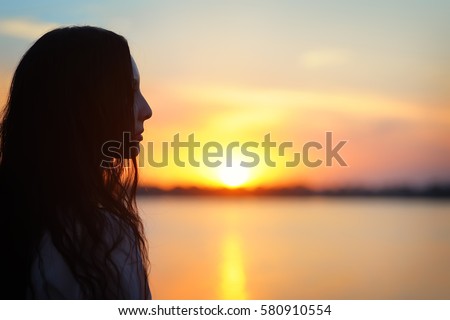 Profile of beautiful Asian woman looking at the sunset.  Silhouette on a background of lake Royalty-Free Stock Photo #580910554