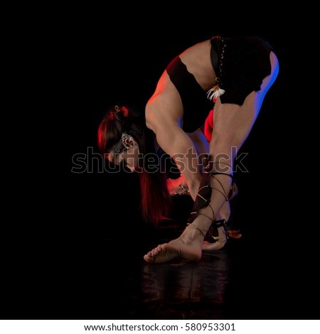 woman athlete gymnast in the form of an elf performs acrobatics on a black background in the scenic red and blue light.