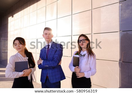 Modern handsome male man and two pretty confident girl, successful young office workers, businessmen, students holding in hands documents, smiling and posing to photographer camera, taking pictures