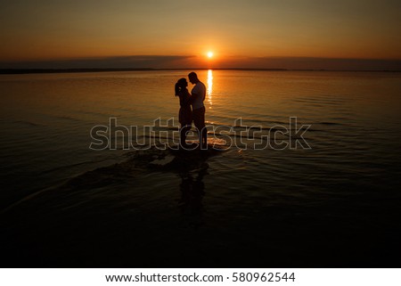 Two young lovers standing on a beach and looking to each other on sunset