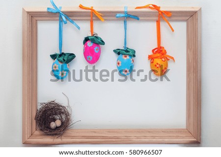 Multicolored Easter eggs in a wooden frame with a white background and a small nest in the corner

