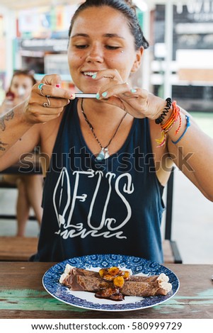 Young woman taking pictures of her breakfast with smartphone before eating sweet pancakes with bananas and creme 