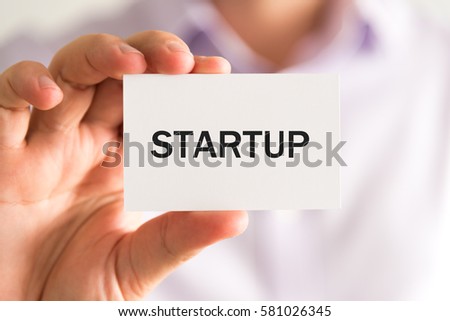 Closeup on businessman holding a card with text STARTUP, business concept image with soft focus background
