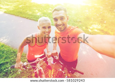 fitness, sport, people, technology and healthy lifestyle concept - happy couple with bicycle taking selfie outdoors