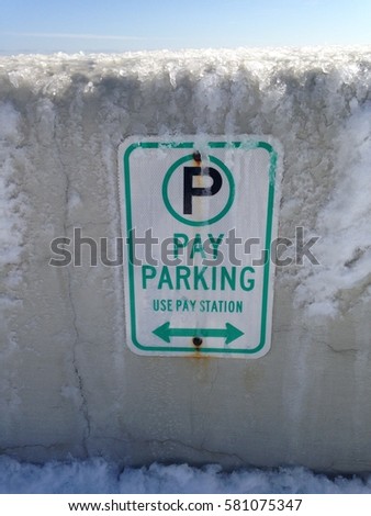Ice covered pay parking sign on the cement sea wall in the winter