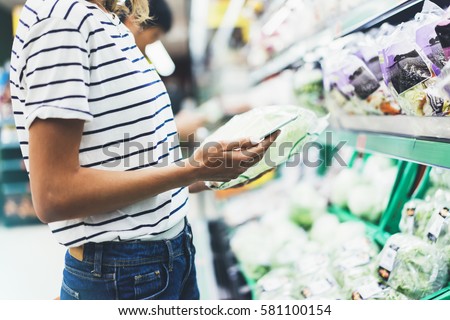 Young woman shopping healthy food in supermarket blur background. Female hands buy products cabbage using smart phone in store. Hipster at grocery using smart phone. Person comparing price of produce