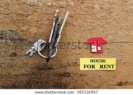 House for rent concept. Rusty keys and a replica of a house on old wooden background with words House For Rent.