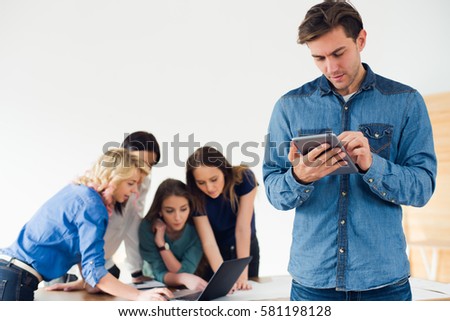 Handsome young designer using his digital tablet in the office with his colleagues in the background