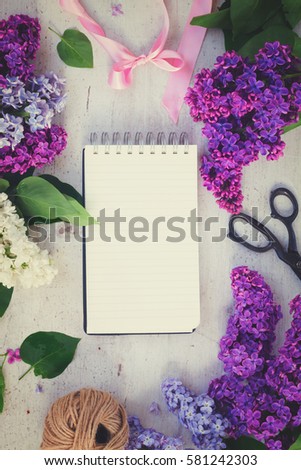 Frame with fresh lilac flowers on white wooden background, copy space on notebook, retro toned