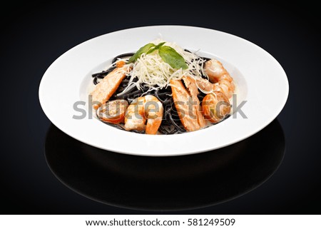 Pasta with shrimp and salmon in a white plate on a black background