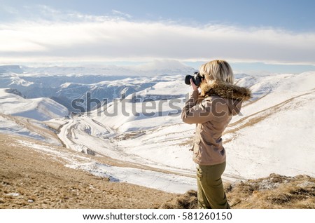 Beautiful blonde girl with a camera to take pictures of Caucasian mountains
