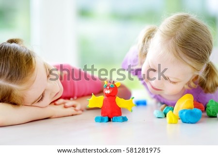 Two cute little sisters having fun together with colorful modeling clay at a daycare. Creative kids molding at home. Kids play with plasticine or dough. 