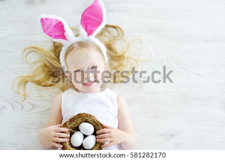 Cute little girl wearing bunny ears playing egg hunt on Easter. Adorable child celebrate Easter at home. 