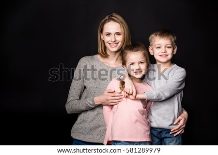 Happy mother with two adorable kids standing embracing isolated on black